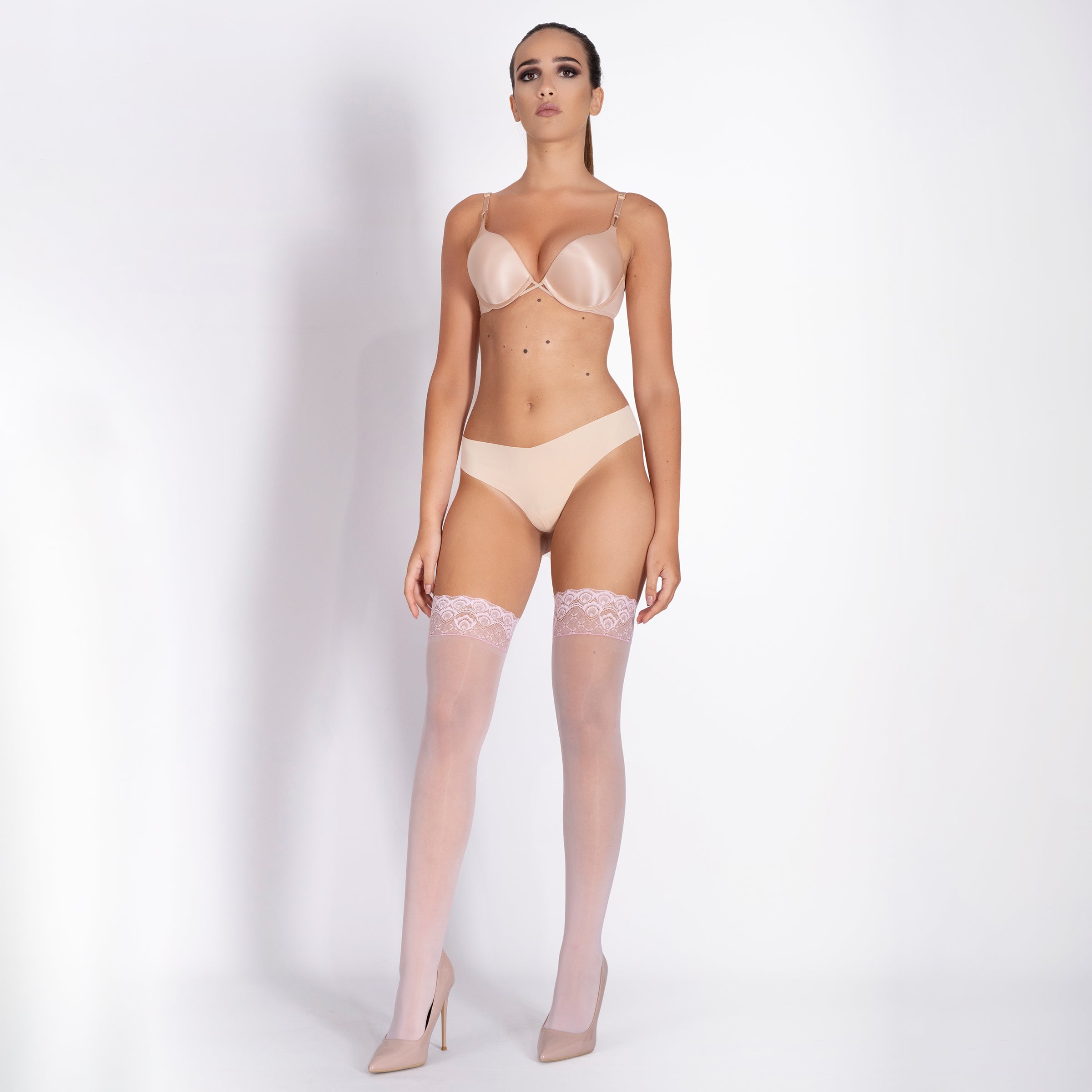 Model wearing a beige lingerie set with stockings on a white background
